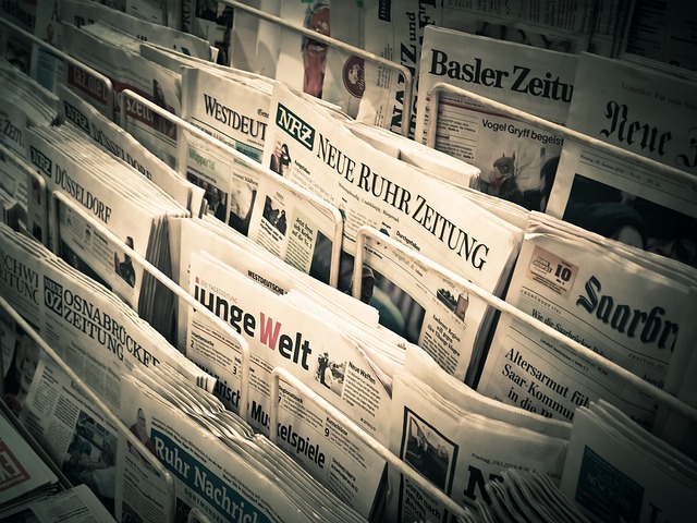 Newspaper racks filled with undated front pages, mostly German-language papers like Neue Ruhr Zeitung and Westdeutsche Allgemeine Zeitung.